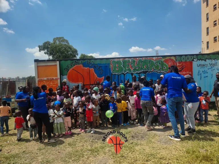 A large group of children and volunteers gather in front of a colourful painted mural in Nairobi