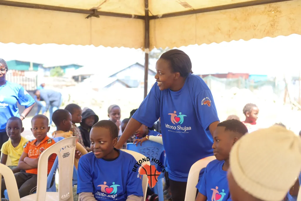 A Mtoto Shujaa volunteer in a blue shirt talks with children seated under a tent in Nairobi