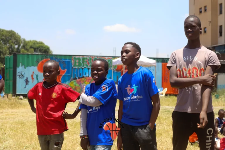 Boys and a volunteer stand together on the grass in front of painted containers in Nairobi