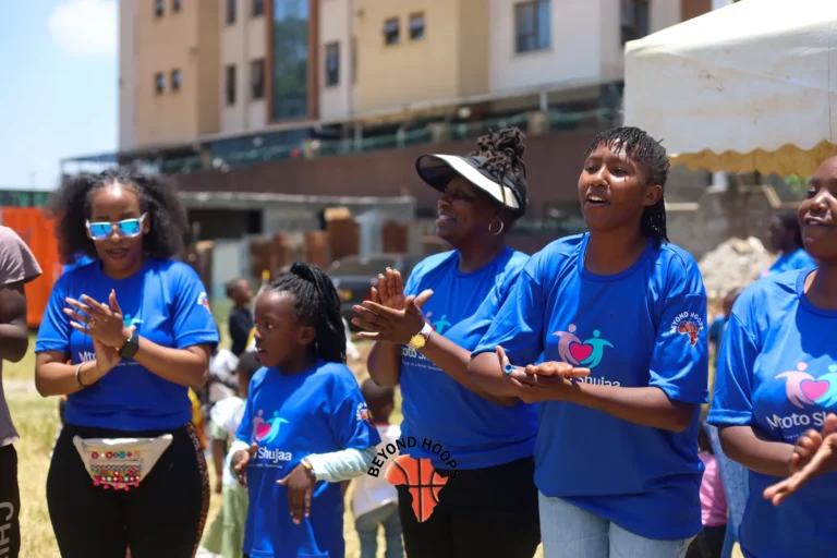 Mtoto Shujaa volunteers in blue shirts clap and smile together at a community event in Nairobi