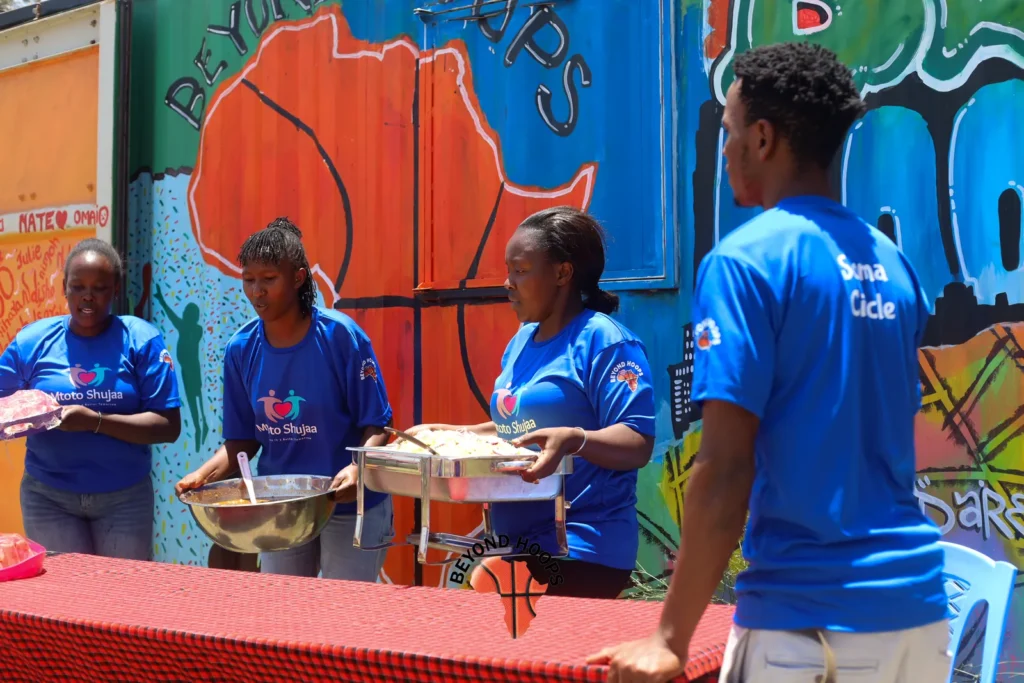 Volunteers serve food from large pots in front of a painted mural during a feeding day in Nairobi