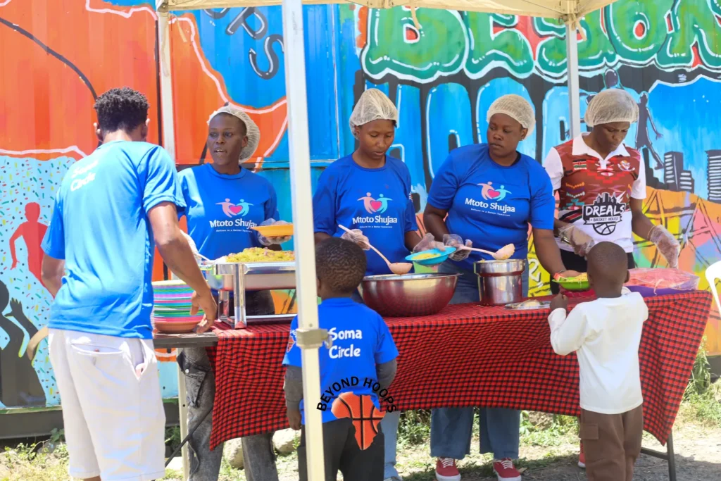 Volunteers prepare and serve meals at a table under a canopy during a feeding day in Nairobi