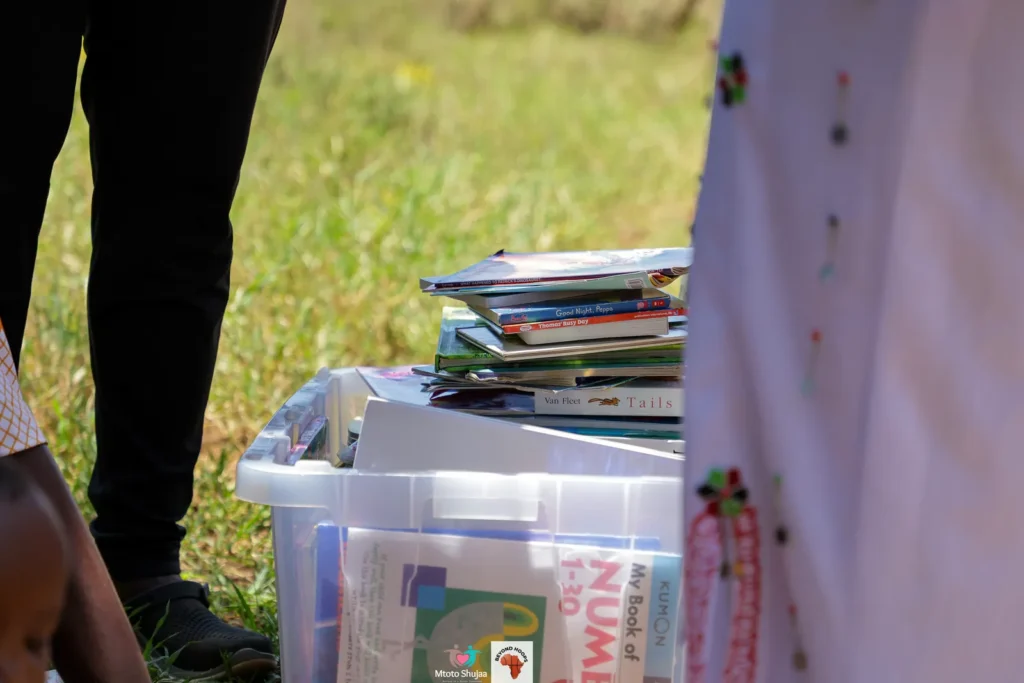 A crate of donated books and learning materials sits on the grass ready to be shared