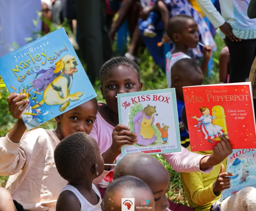 Children proudly hold up donated storybooks during a Mtoto Shujaa reading session in Kenya