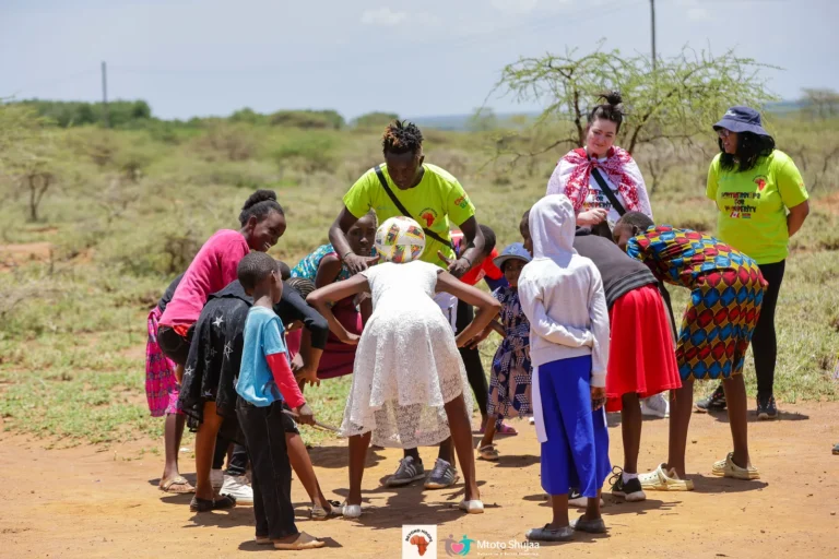 Volunteers and children play a lively circle game on dusty open ground in Kenya