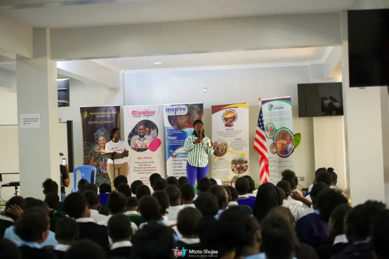 An audience listens to a presentation beside programme banners at a community forum in Kenya