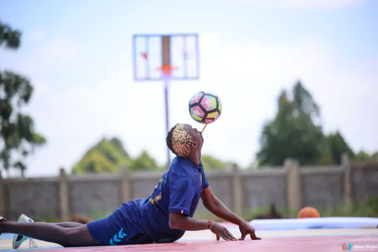 A player in blue balances a basketball while stretched out on an outdoor court in Kenya