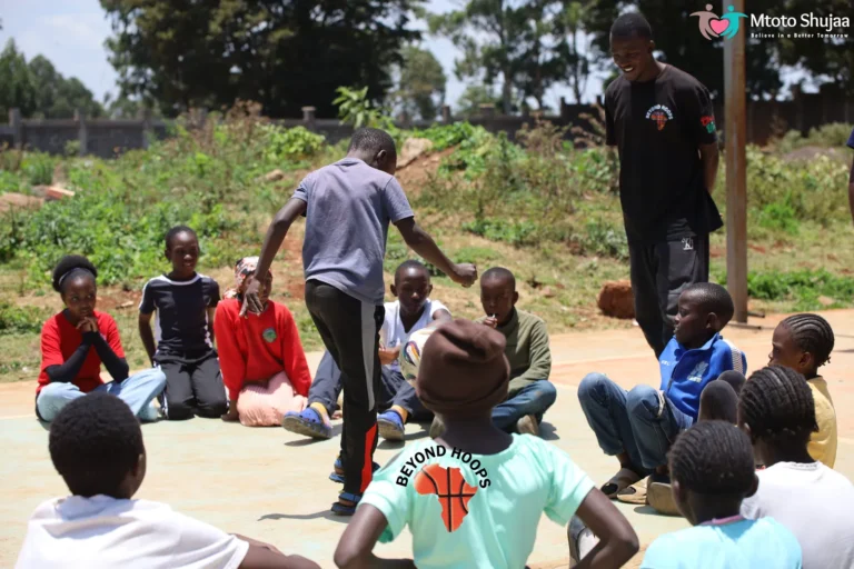 A coach leads a group of children seated on an outdoor court during a sports session in Kenya