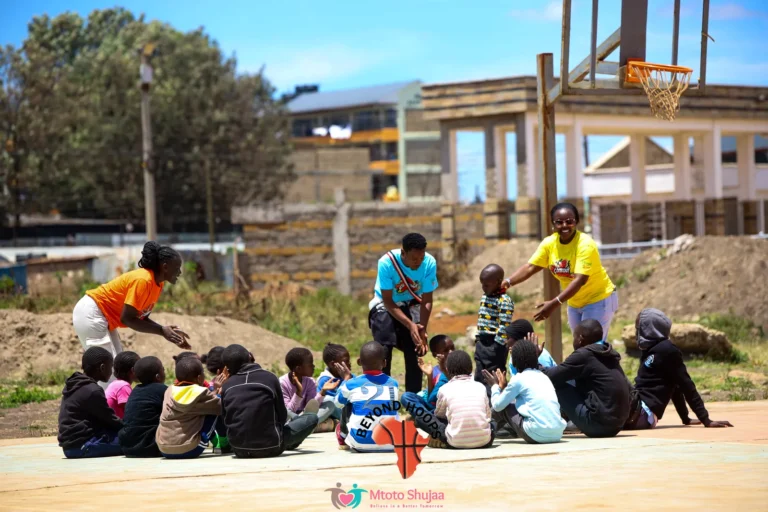 Children sit on a court as coaches lead a basketball session beneath the hoops in Kenya